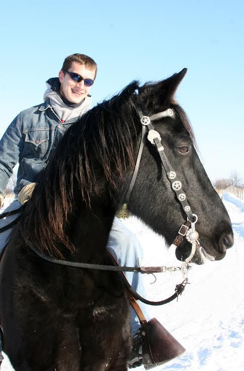 Person in sunglasses riding a black horse in a snowy landscape