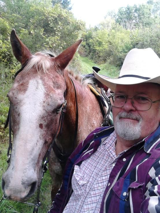 Man in white cowboy hat posing beside a brown horse outdoors.