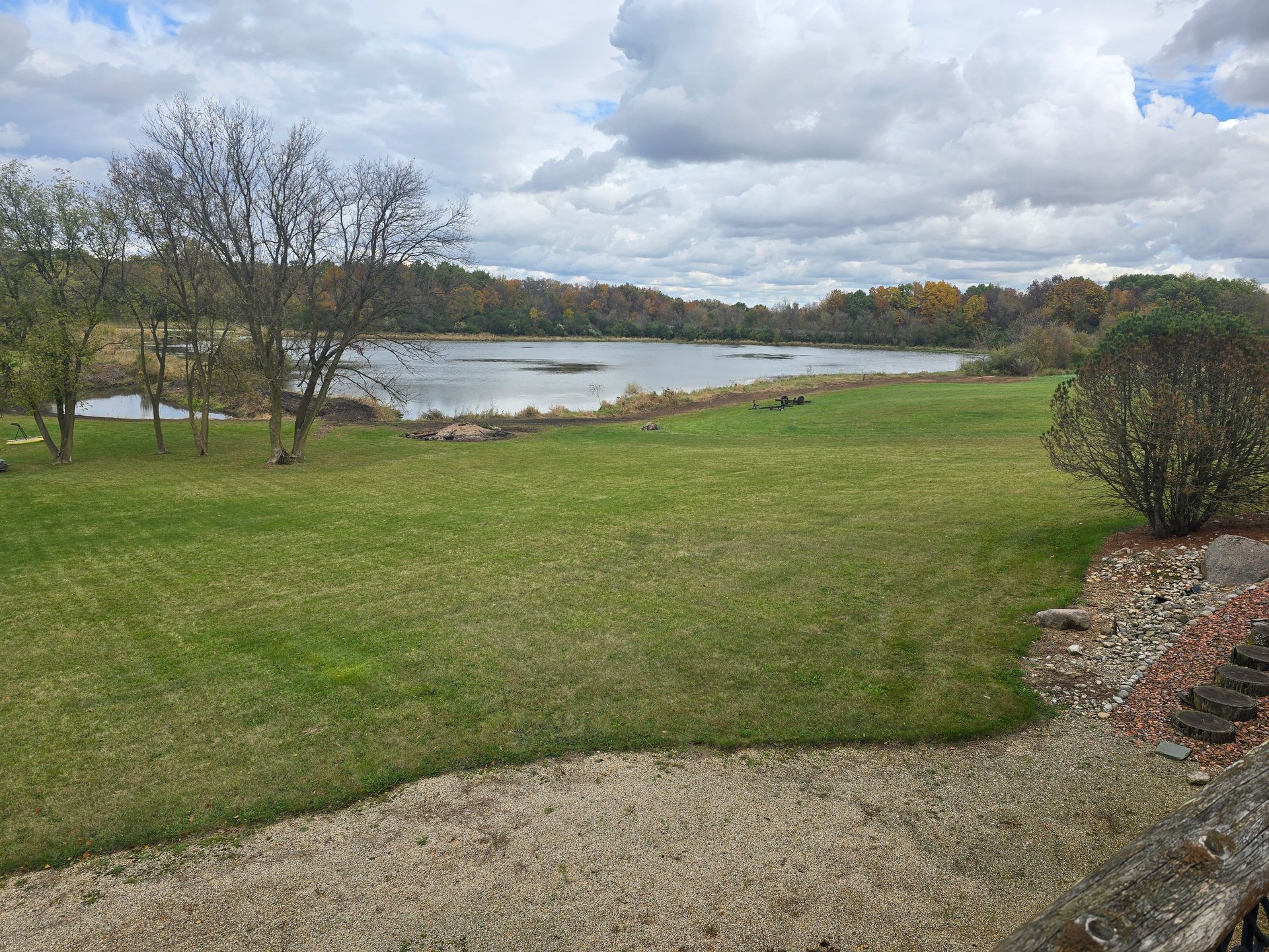 Grassy park with a pond, cloudy sky, bare trees, and a stone path in the foreground