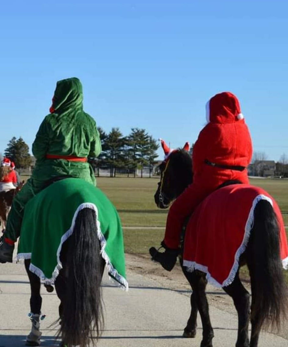 Two riders on horses wearing red and green costumes in an outdoor field.