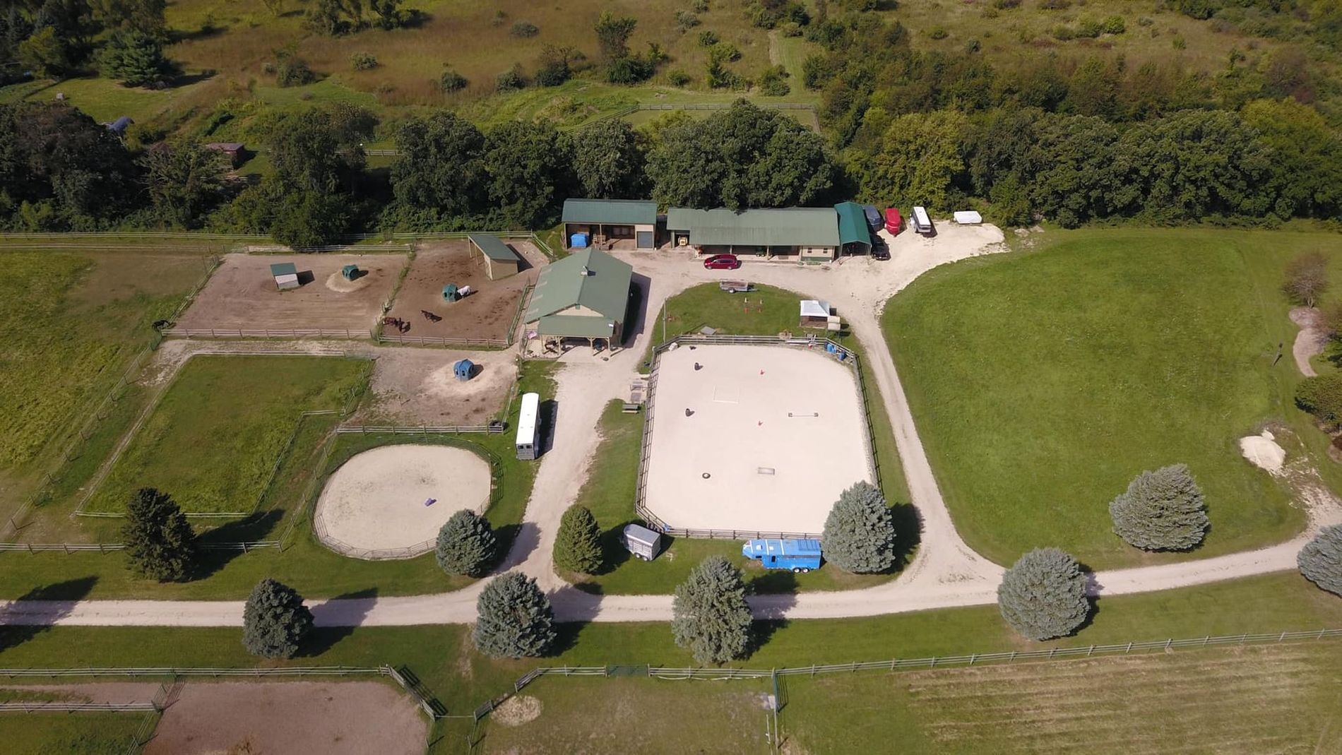 Aerial view of a rural park with playgrounds, paths, grassy fields, and trees along the edge.