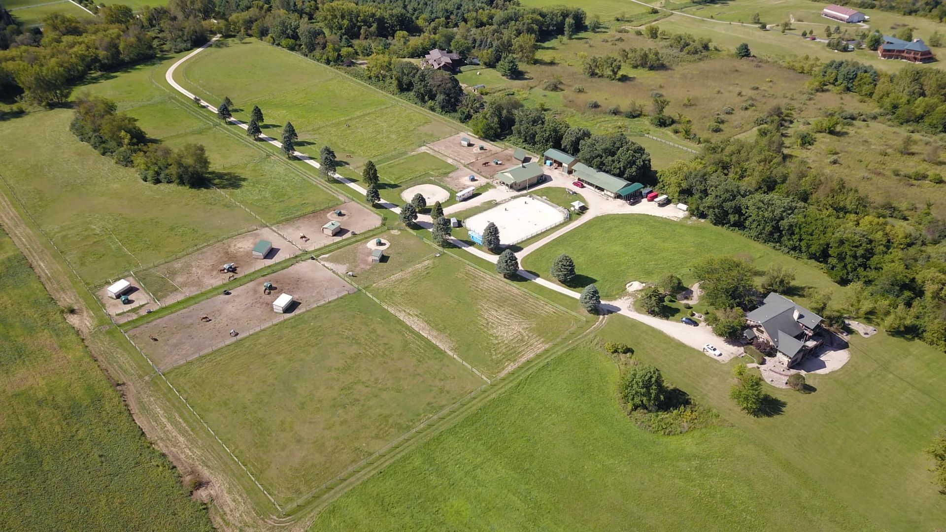 Aerial view of a rural property with buildings, driveways, fields, and trees.