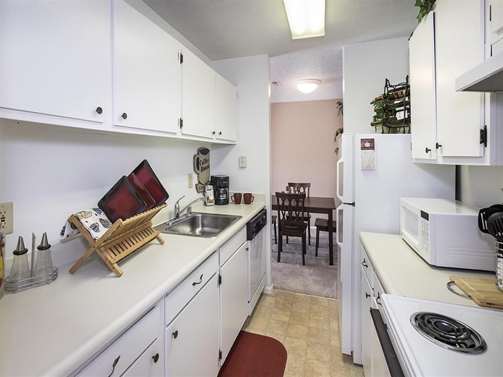 White kitchen with upper cabinets, sink, and appliances; dining area visible in the back at Shadow Hill, offering apartments in Sharonville, OH.