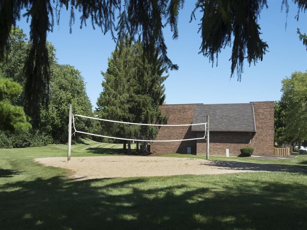 Outdoor sand volleyball court with a net in front of a brick building and tall trees at Shadow Hill, offering apartments near Cincinnati,OH.