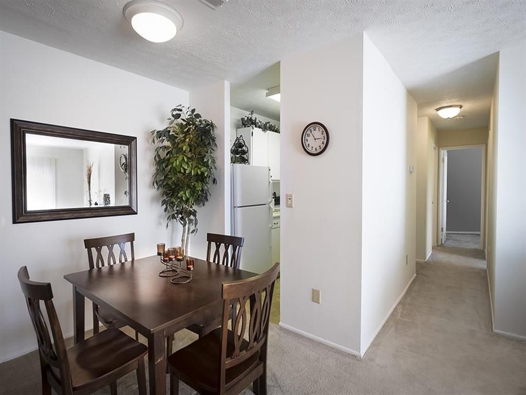Dining area with dark wood table, four chairs, mirror, plant, and hallway to kitchen at Shadow Hill, offering apartments in Sharonville, OH.
