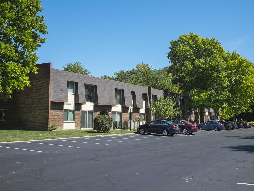 Exterior view of a brick apartment building with a large parking lot and green trees at Shadow Hill, offering pet-friendly townhomes near Cincinnati,OH.