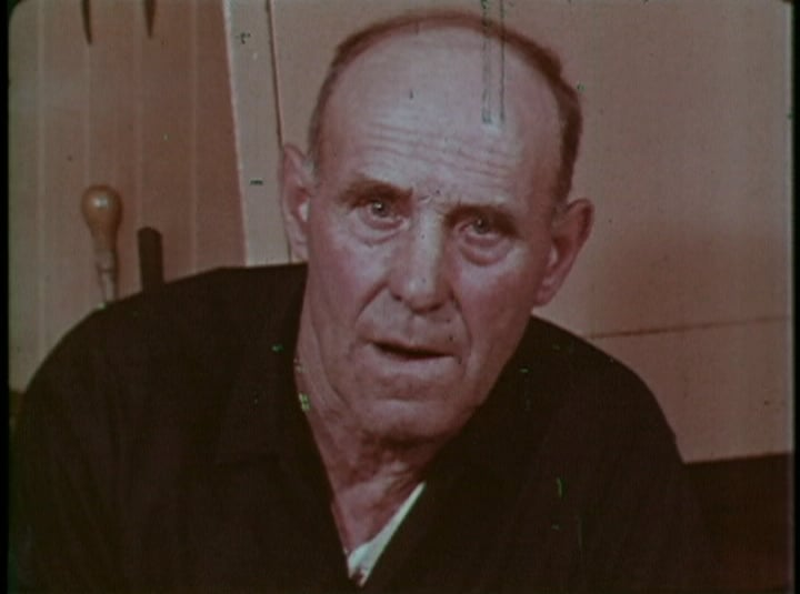 An older man is sitting in a chair and looking at the camera.