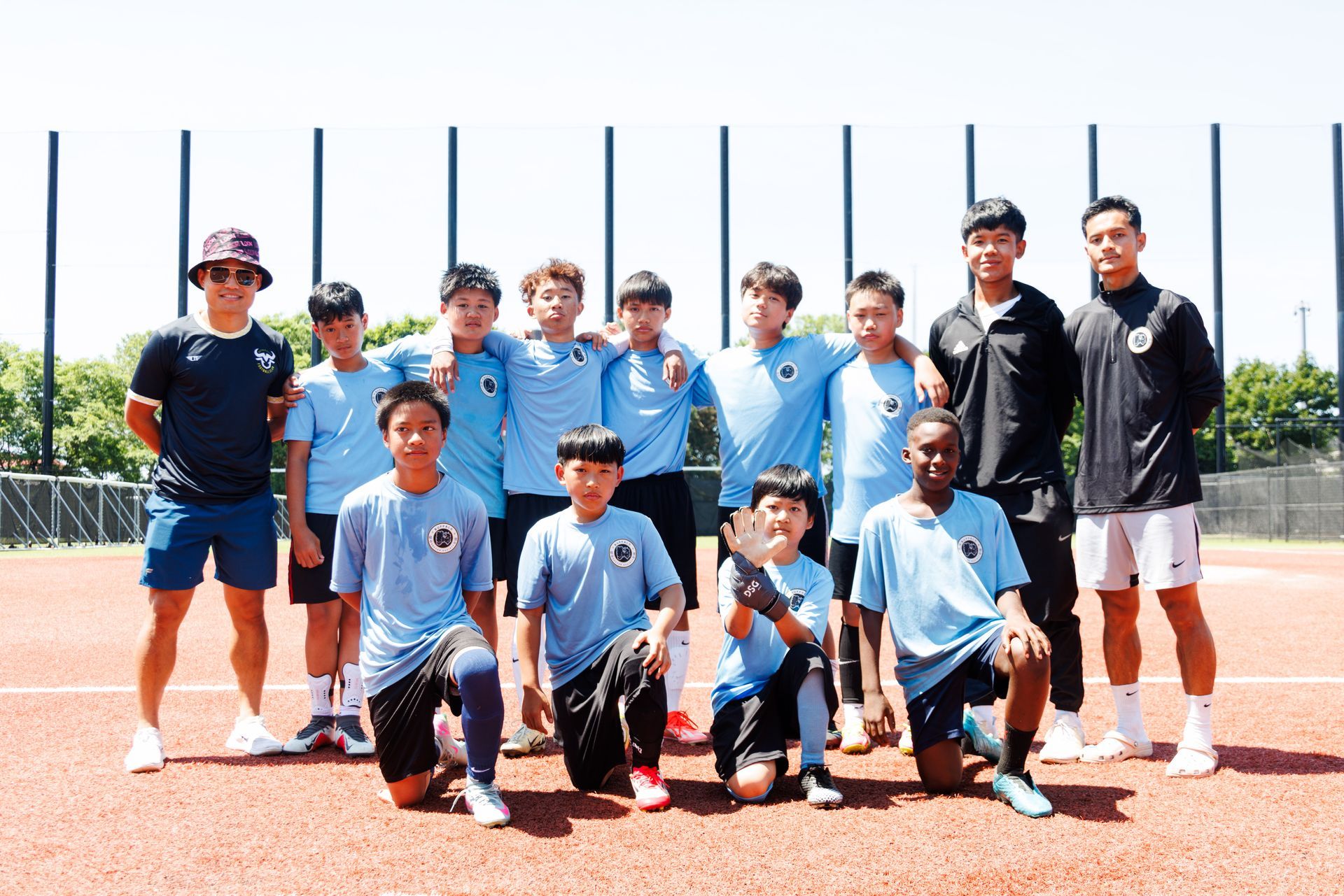 Soccer team posing on a field, wearing light blue and black uniforms in bright sunlight