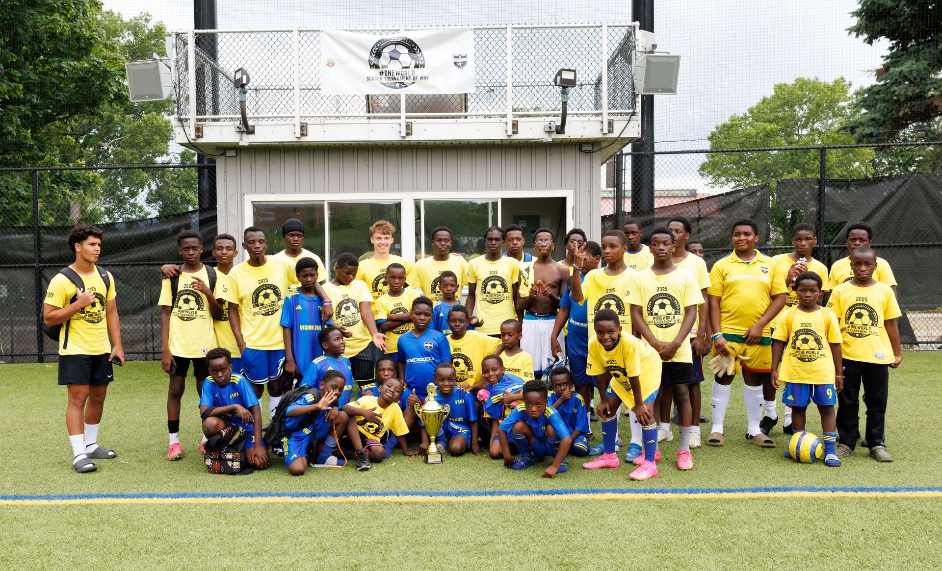 Youth soccer team posing on a field in yellow and blue uniforms in front of a building