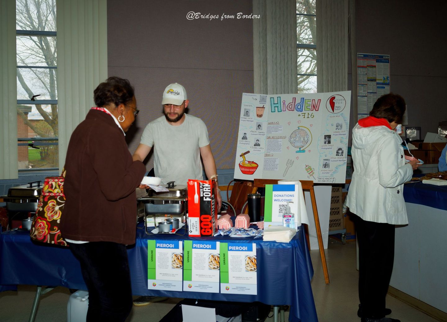 People at a table with product boxes and posters at an indoor informational booth.