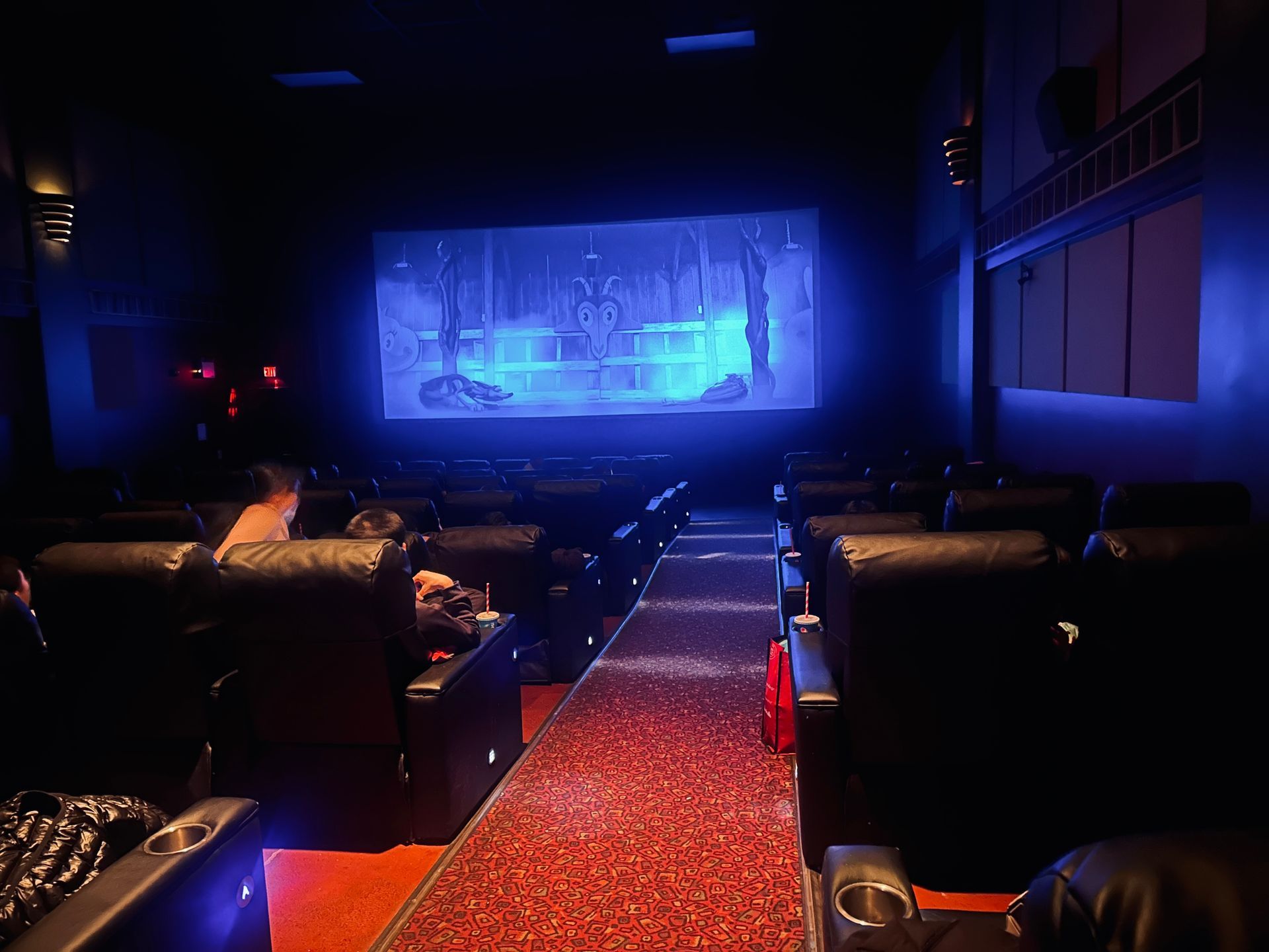 Dark movie theater with red carpet aisle and a blue-lit screen at the front