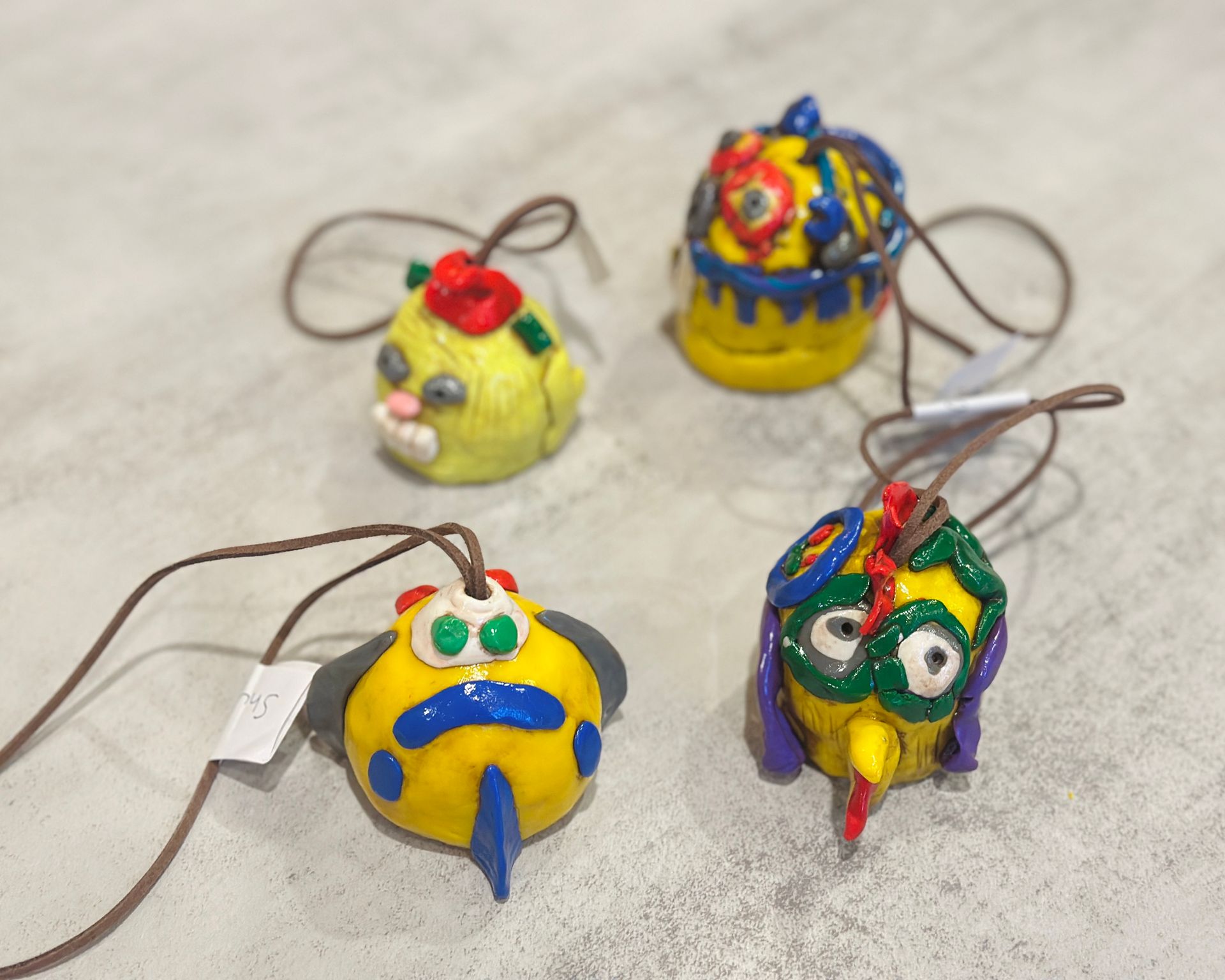 Colorful handmade clay ornaments with looped strings on a light tabletop.