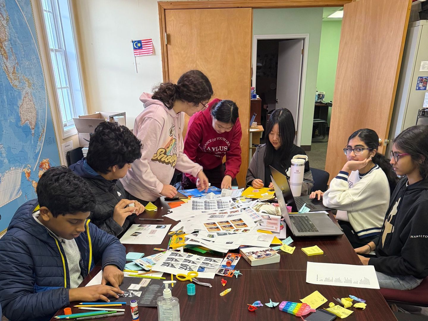 People gathered around a table in a classroom, sorting paper pieces and supplies together.
