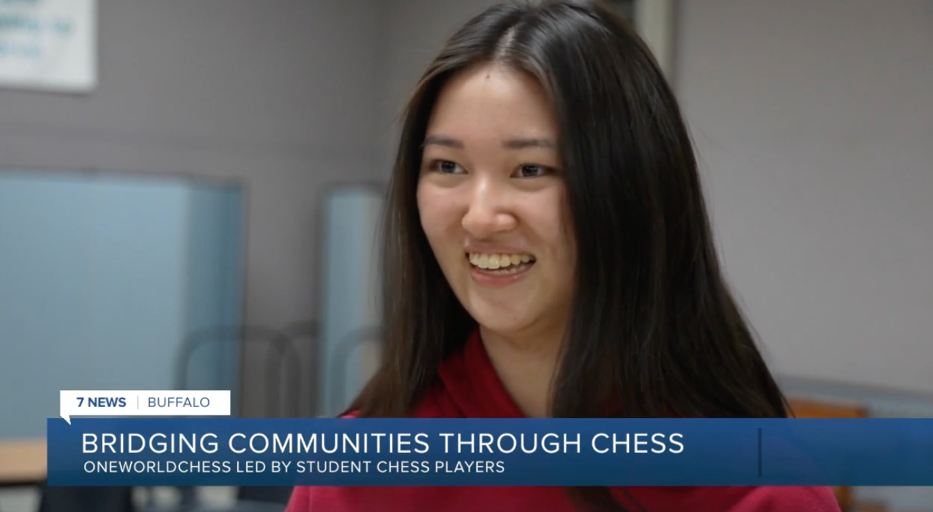 Smiling woman in a classroom with a banner reading “Bridging Communities Through Chess”