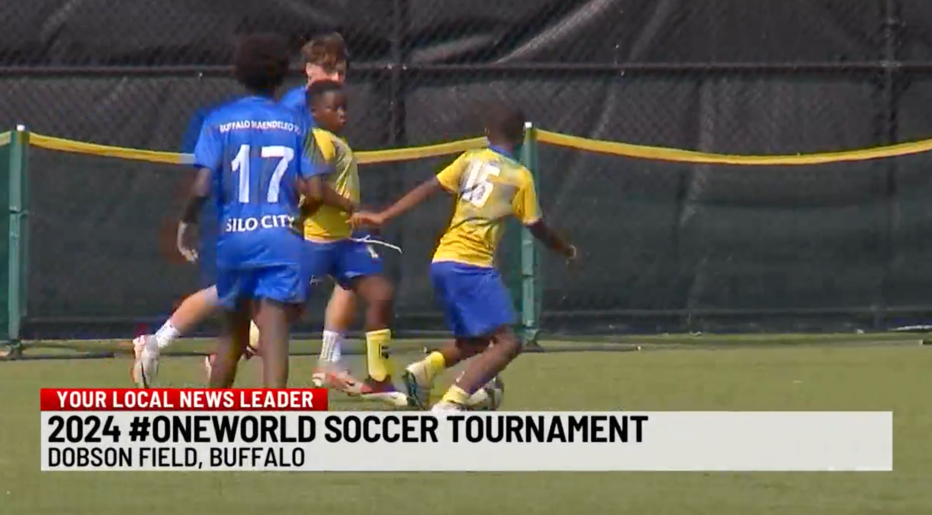 Youth soccer players in blue and yellow battle for the ball at 2024 #ONEWORLD tournament in Buffalo.