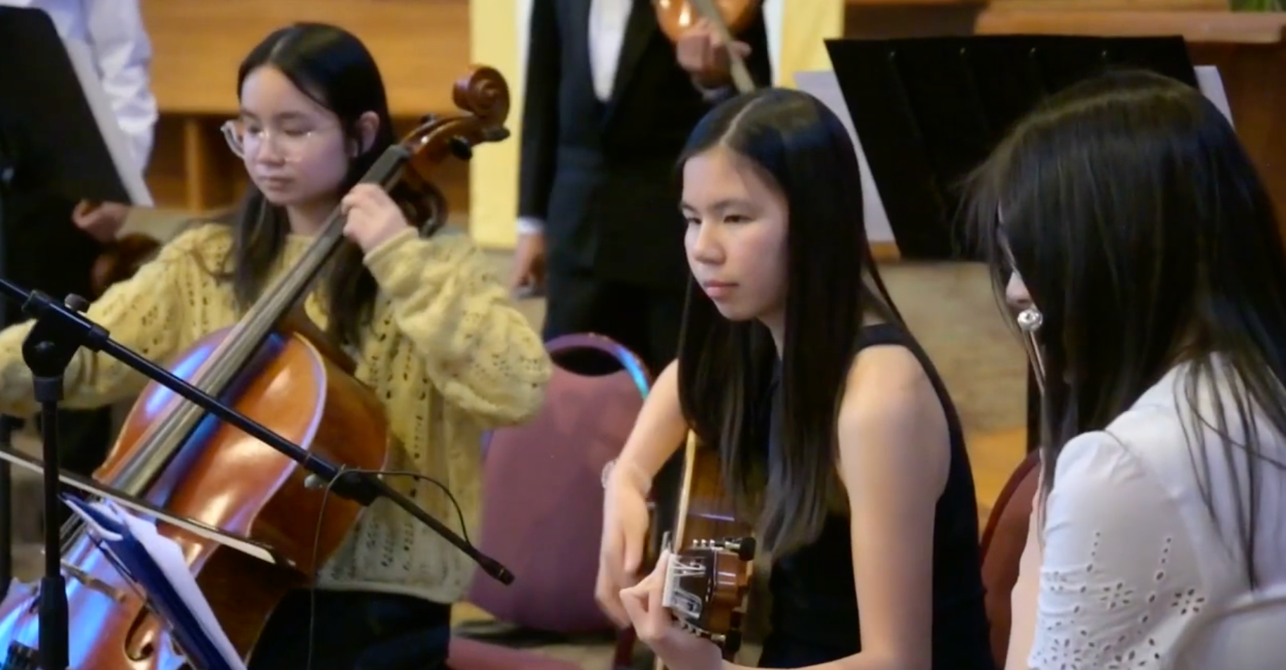 Three young musicians rehearsing, two with guitars and one playing cello in a classroom