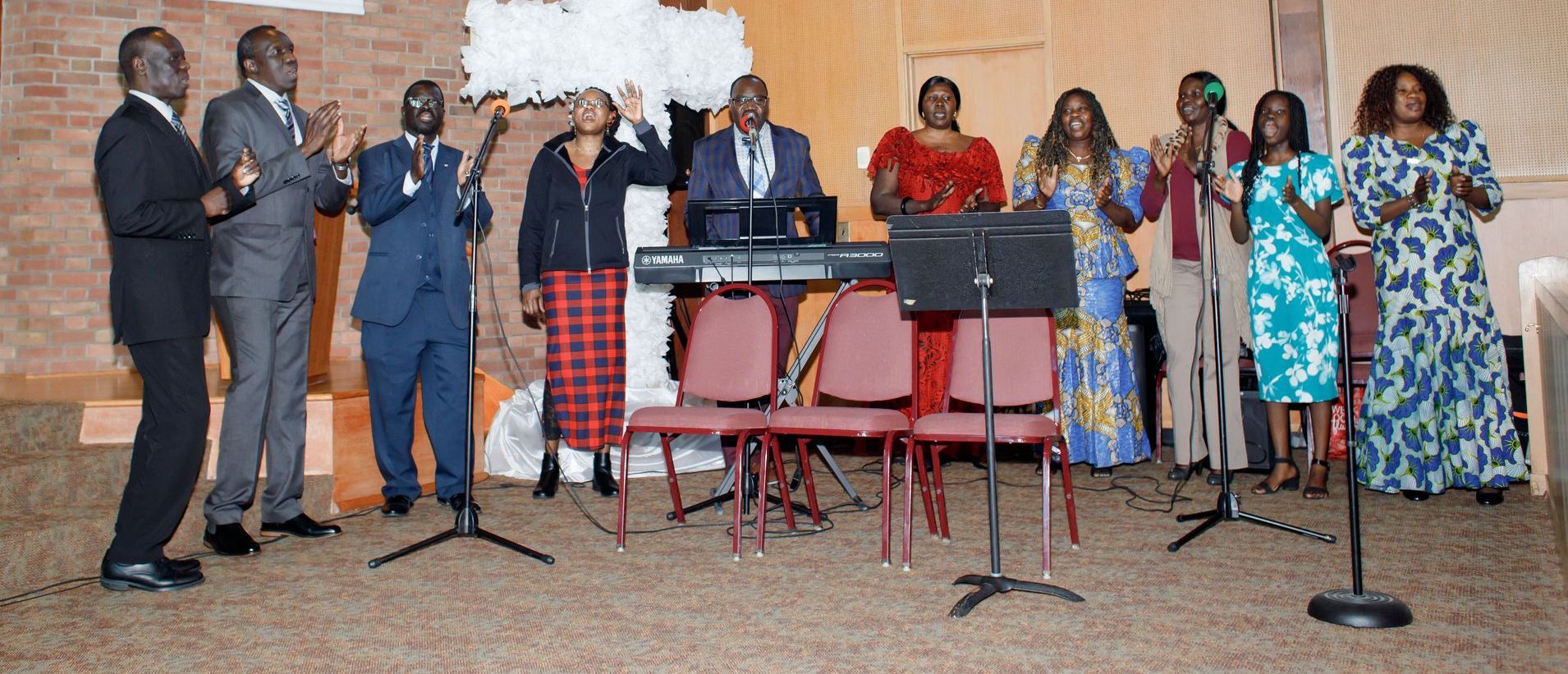 People standing on a stage during a formal event, with microphones, chairs, and a table in front of them.