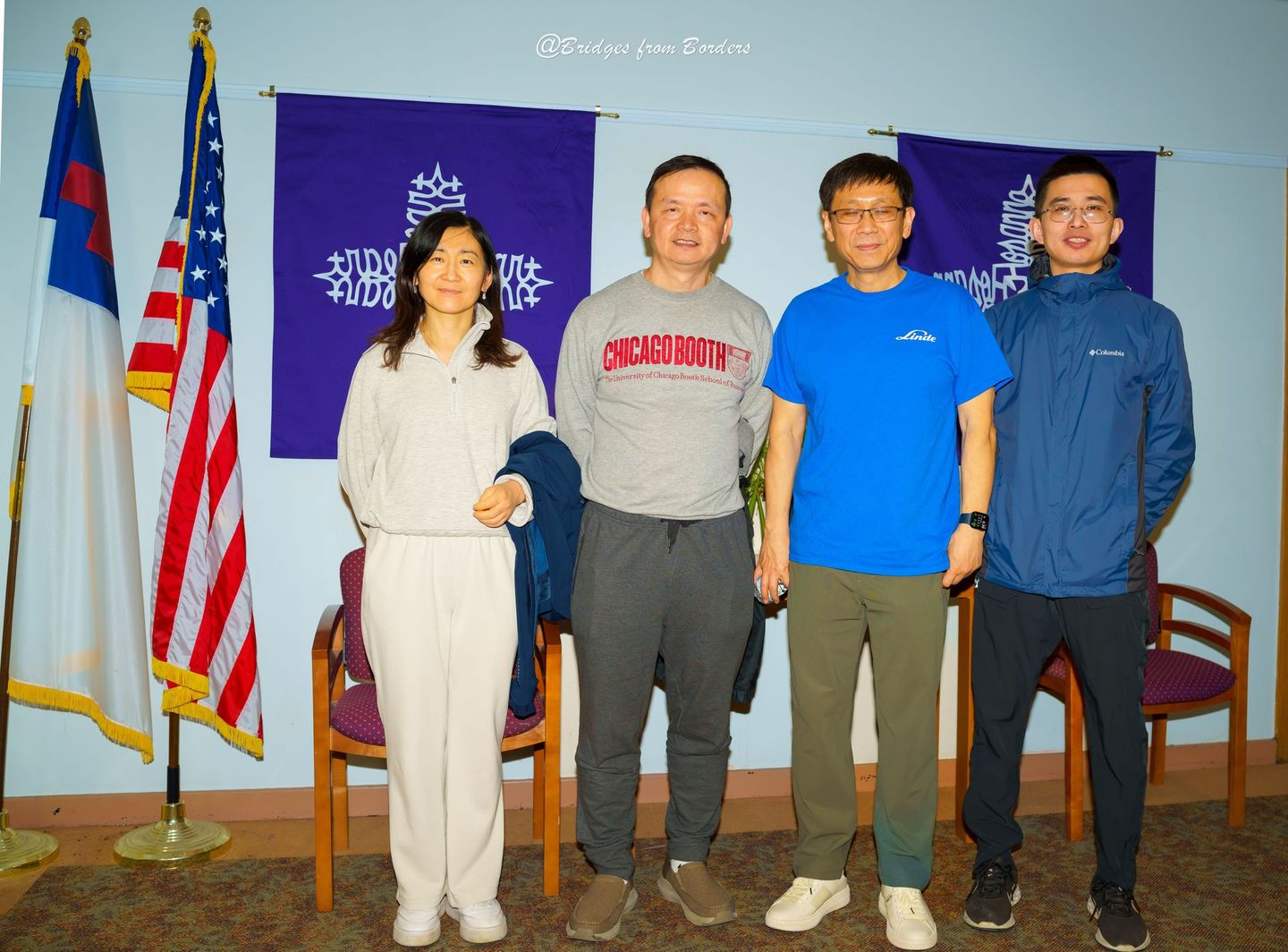 Four people posing indoors in front of flags and a blue backdrop