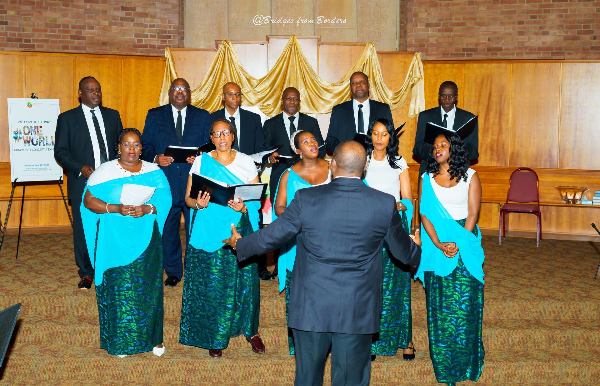 Choir performing on a stage with conductor, formal attire, and gold drapes backdrop