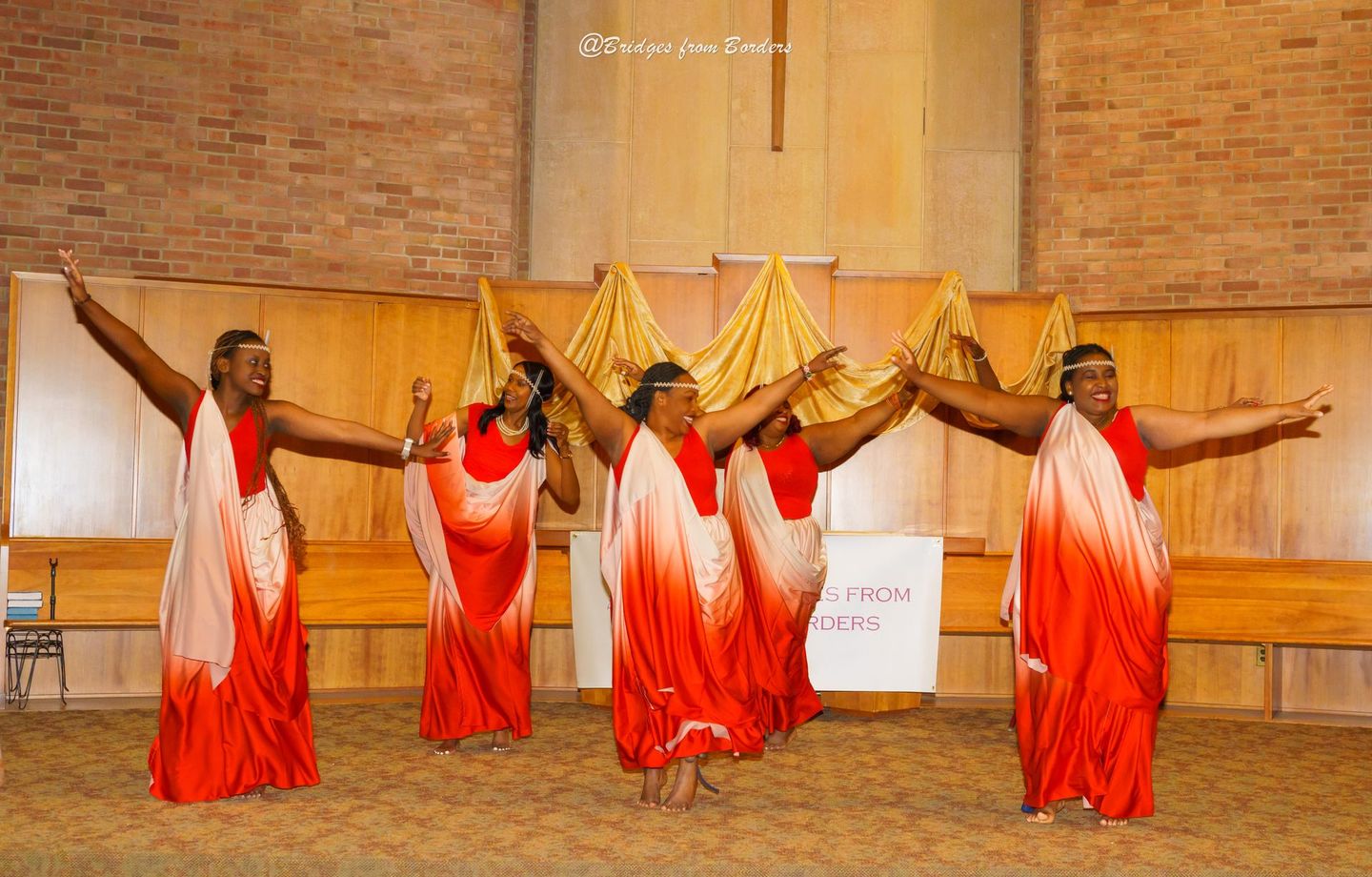 Five dancers in red and white dresses performing on a church stage