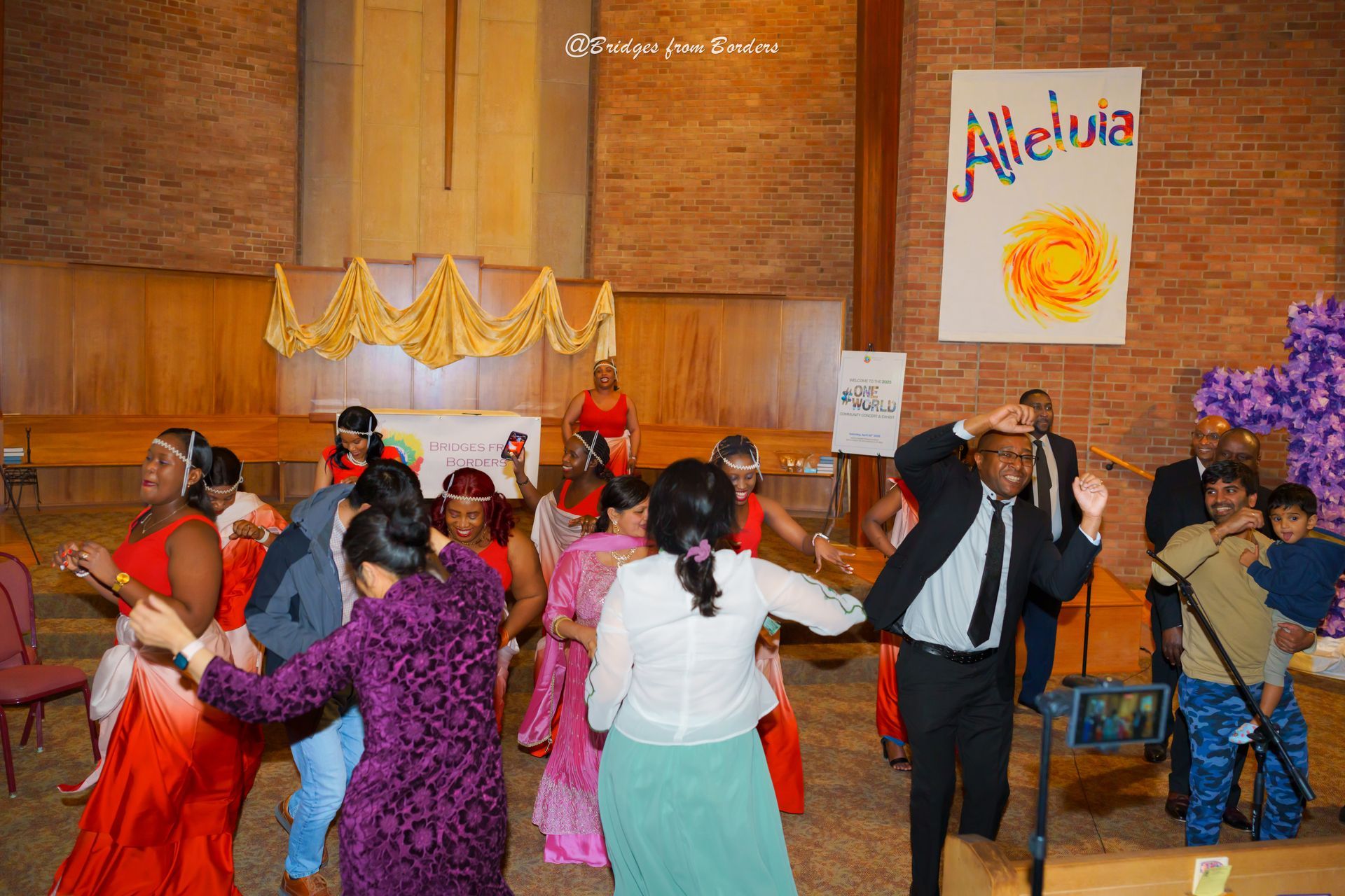 People dancing and singing in a church hall with a “Hallelujah” banner and musicians on stage