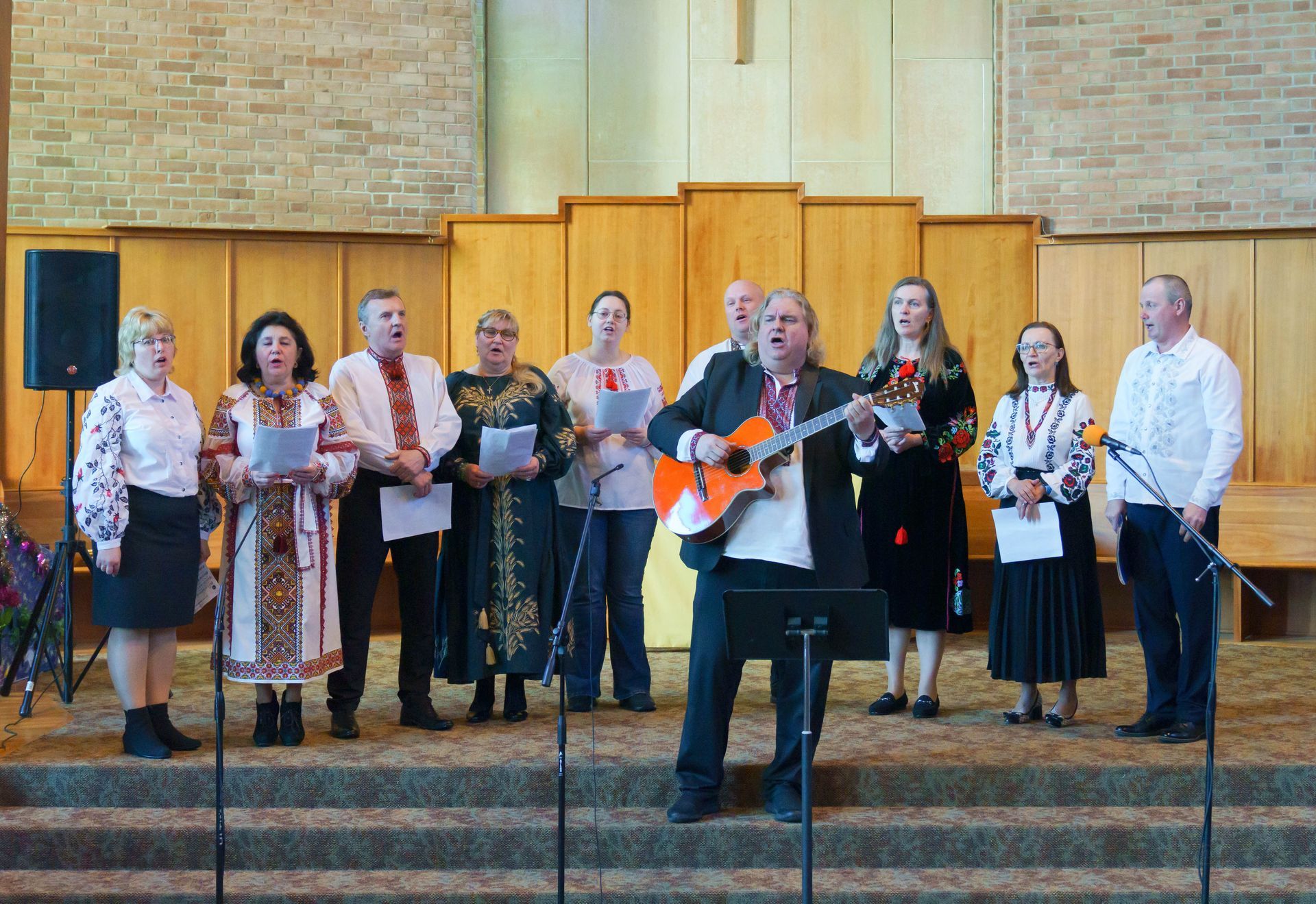 A choir performs in a church, with a guitarist and singers standing on a stage.