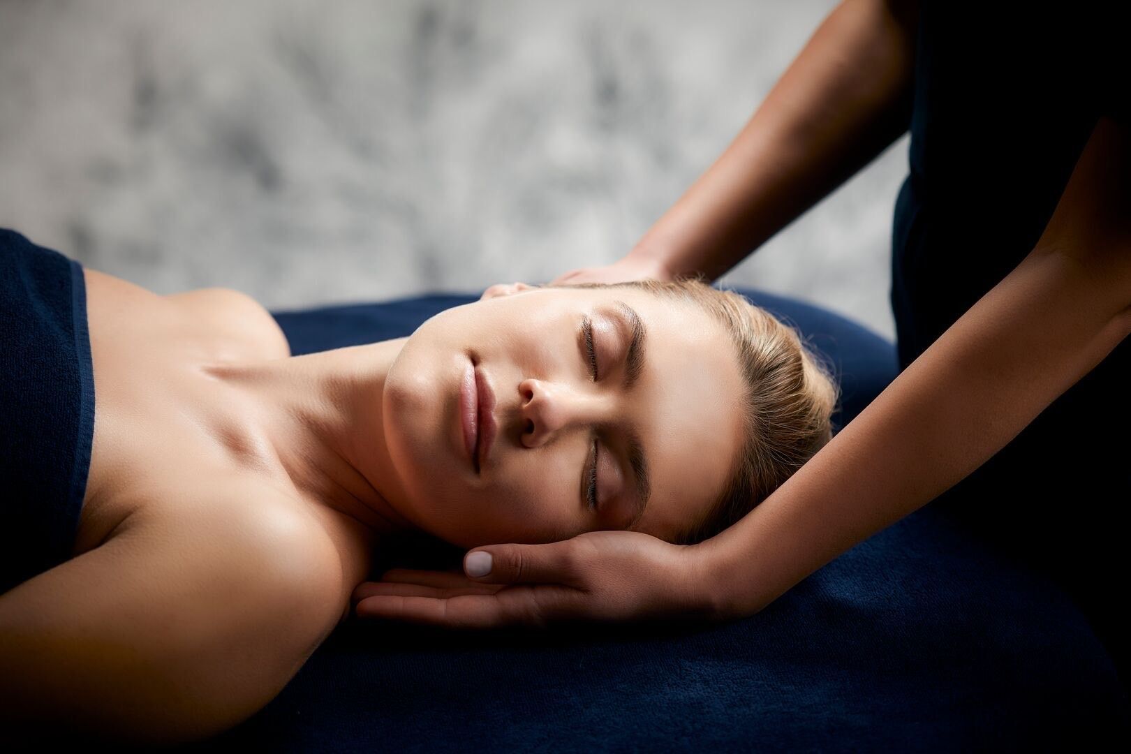Une femme avec une serviette enroulée autour de sa tête reçoit un massage du visage.
