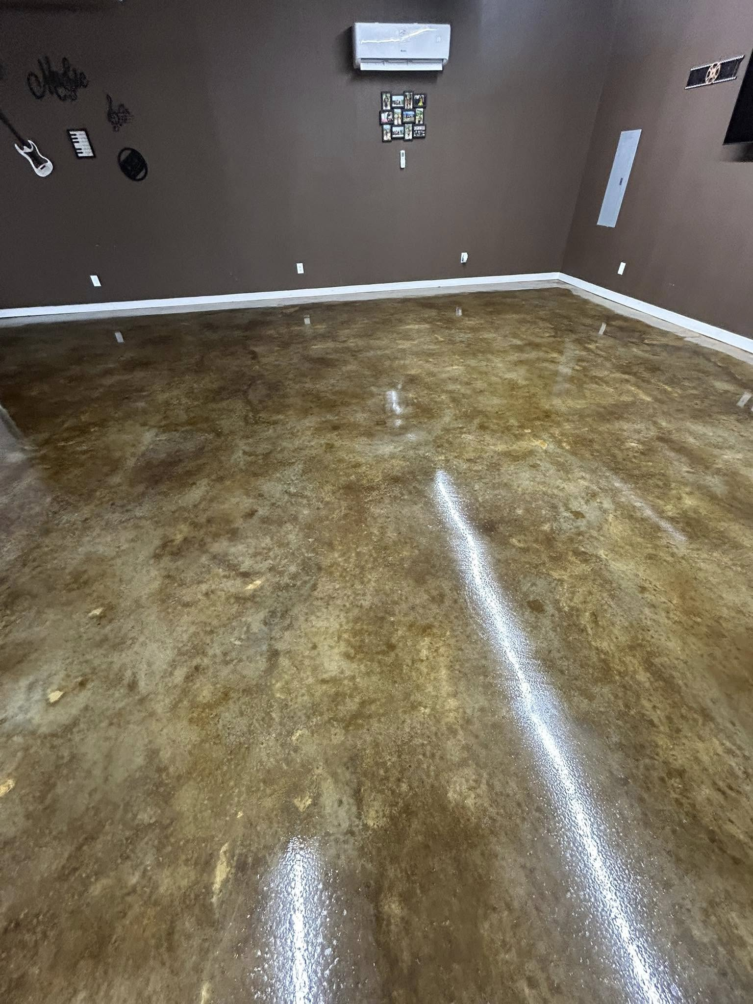 A wide, polished, mottled brown concrete floor in a room with dark brown walls, baseboards, and a wall-mounted mini-split.