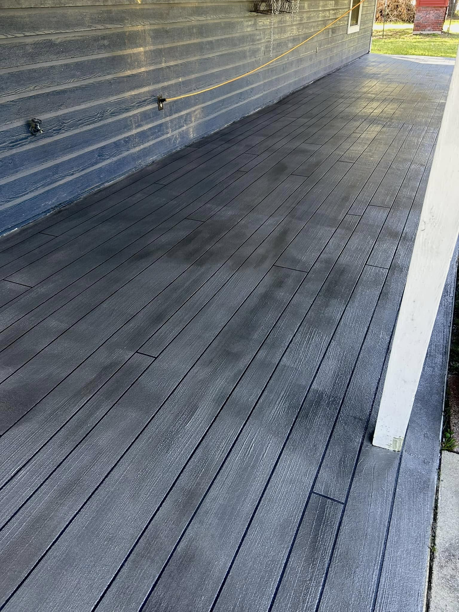 A dark gray wooden deck with visible screw patterns along the boards, adjacent to a gray siding wall.