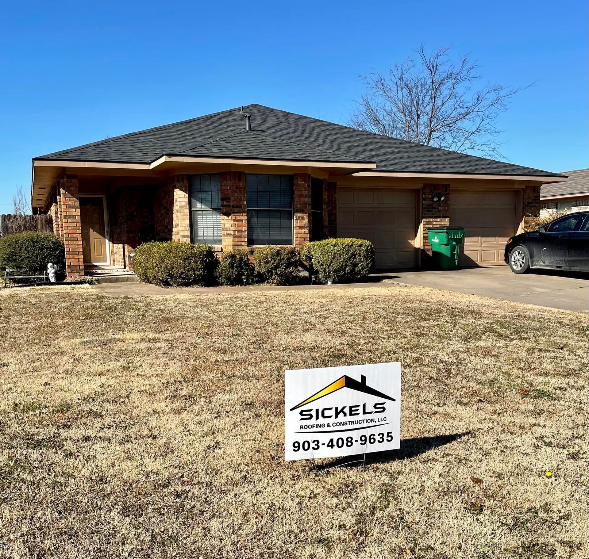 A single-story brick house with a dark shingled roof, a front lawn, and a Sickels Home Construction sign in the yard.