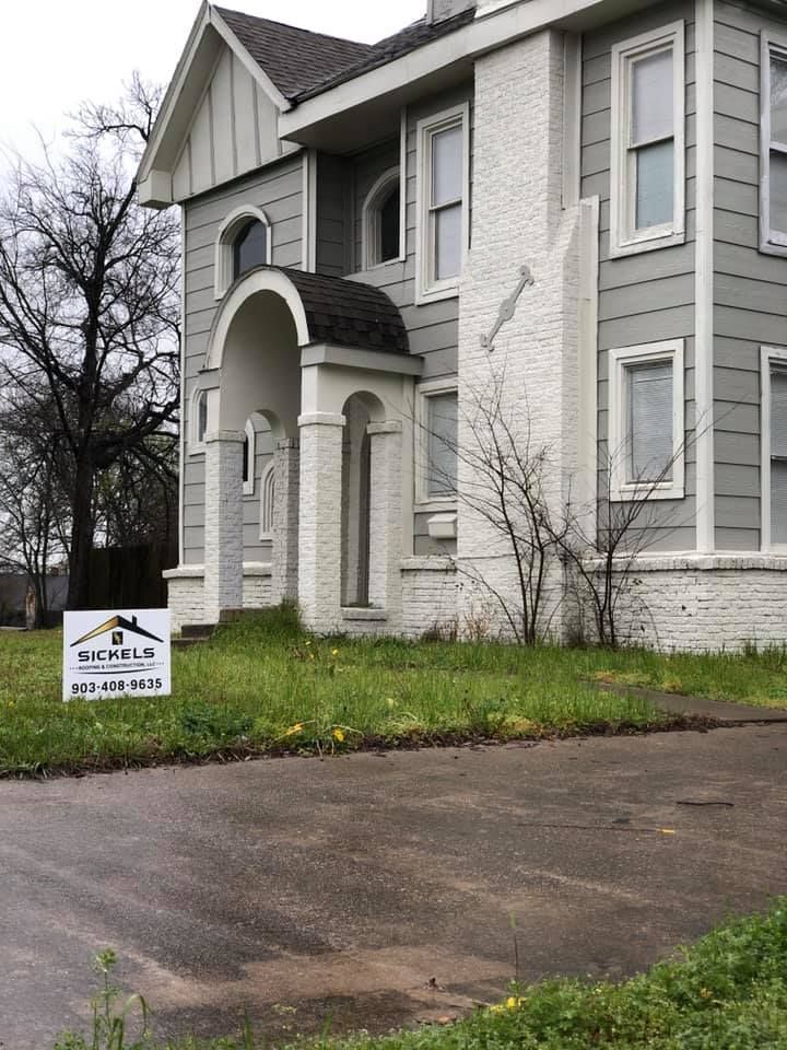 A two-story grey and white house with a arched porch and a real estate sign in the front yard.