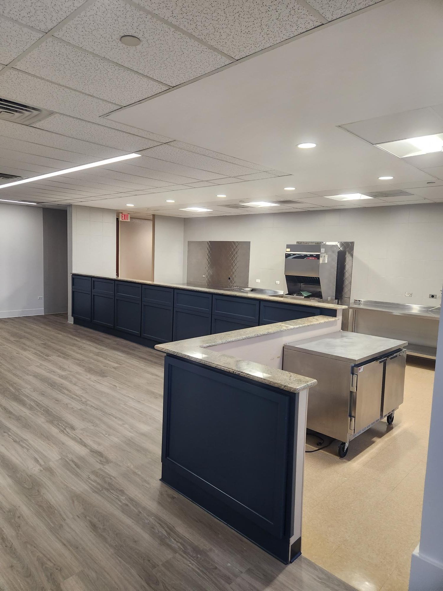 A large empty kitchen with stainless steel appliances and wooden floors.