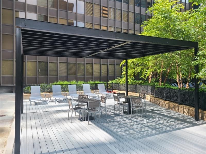 A patio with tables and chairs under a pergola in front of a building - Elgin, IL - Omni Commercial Group, Inc