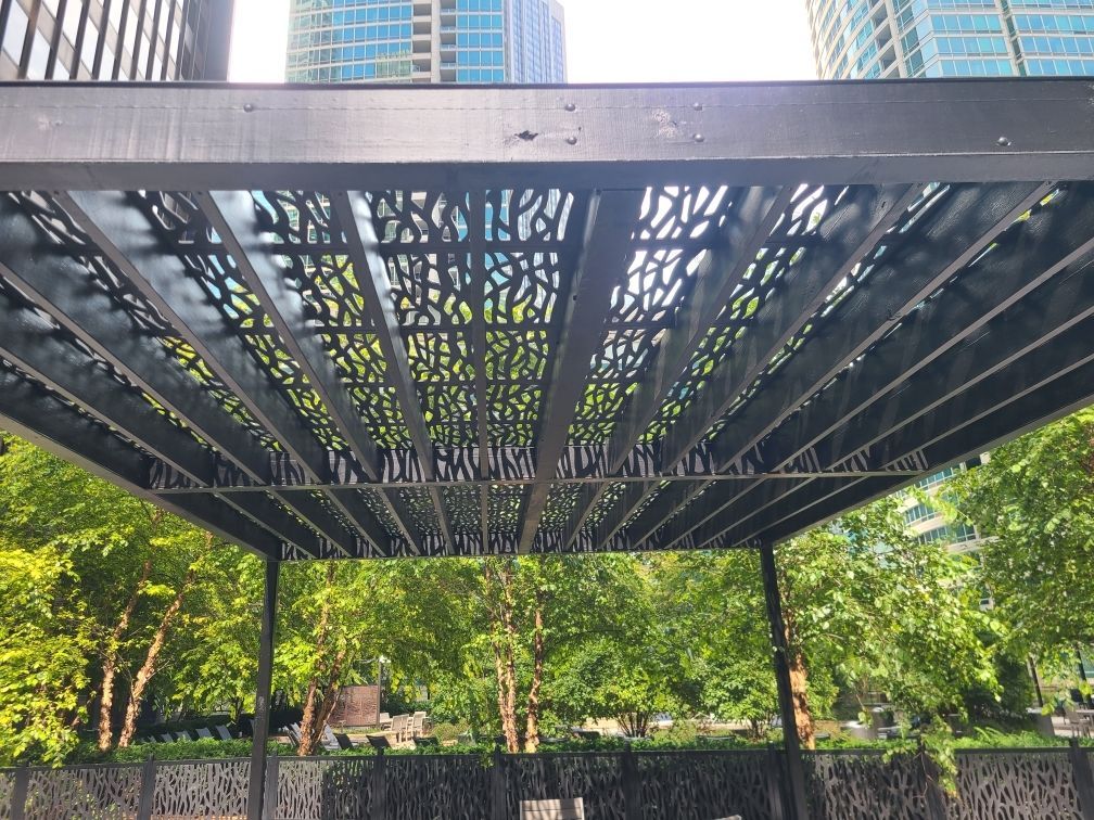 A pergola in a park with trees and buildings in the background.
