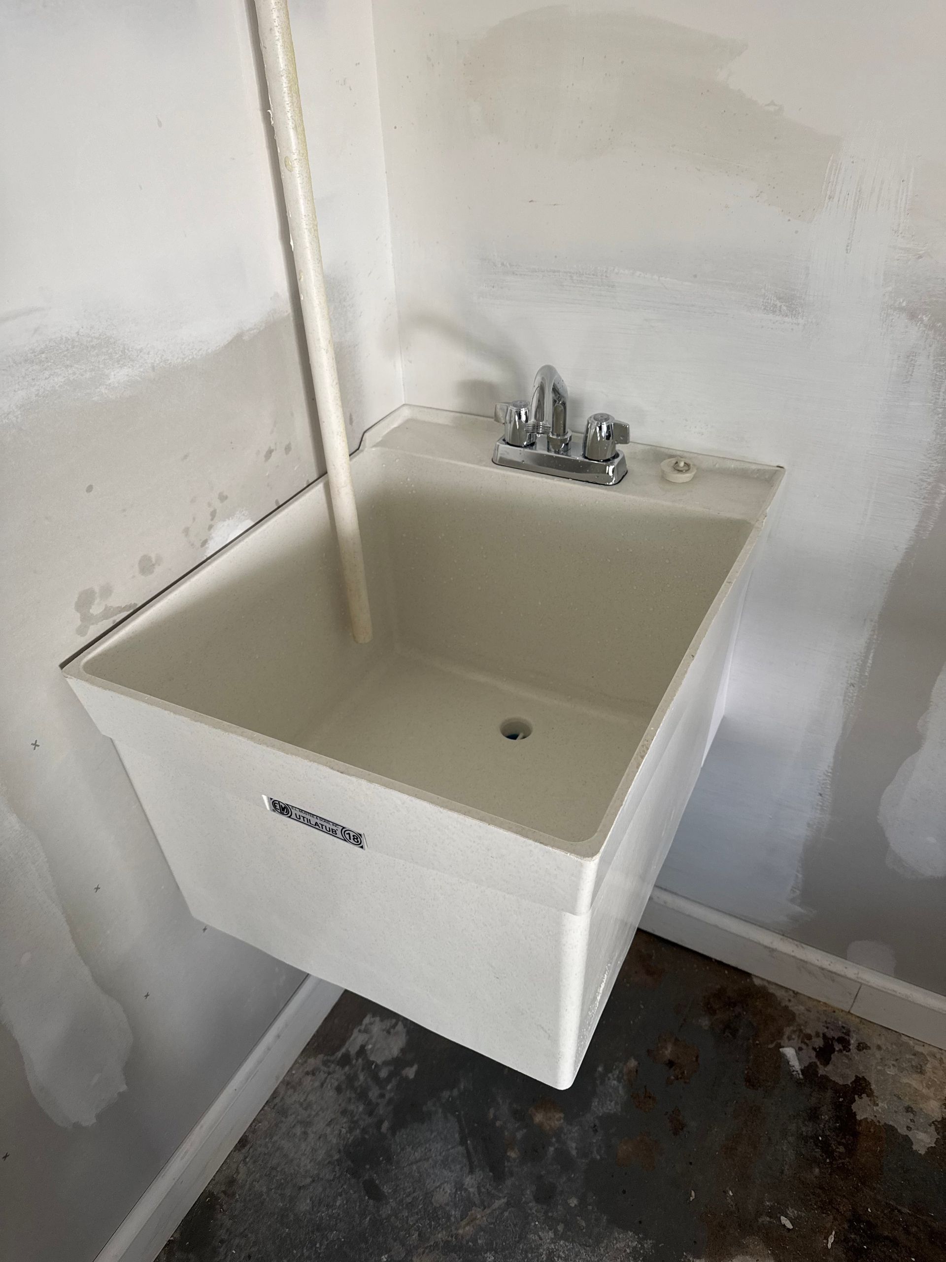 A white laundry sink is hanging on a wall in a room.