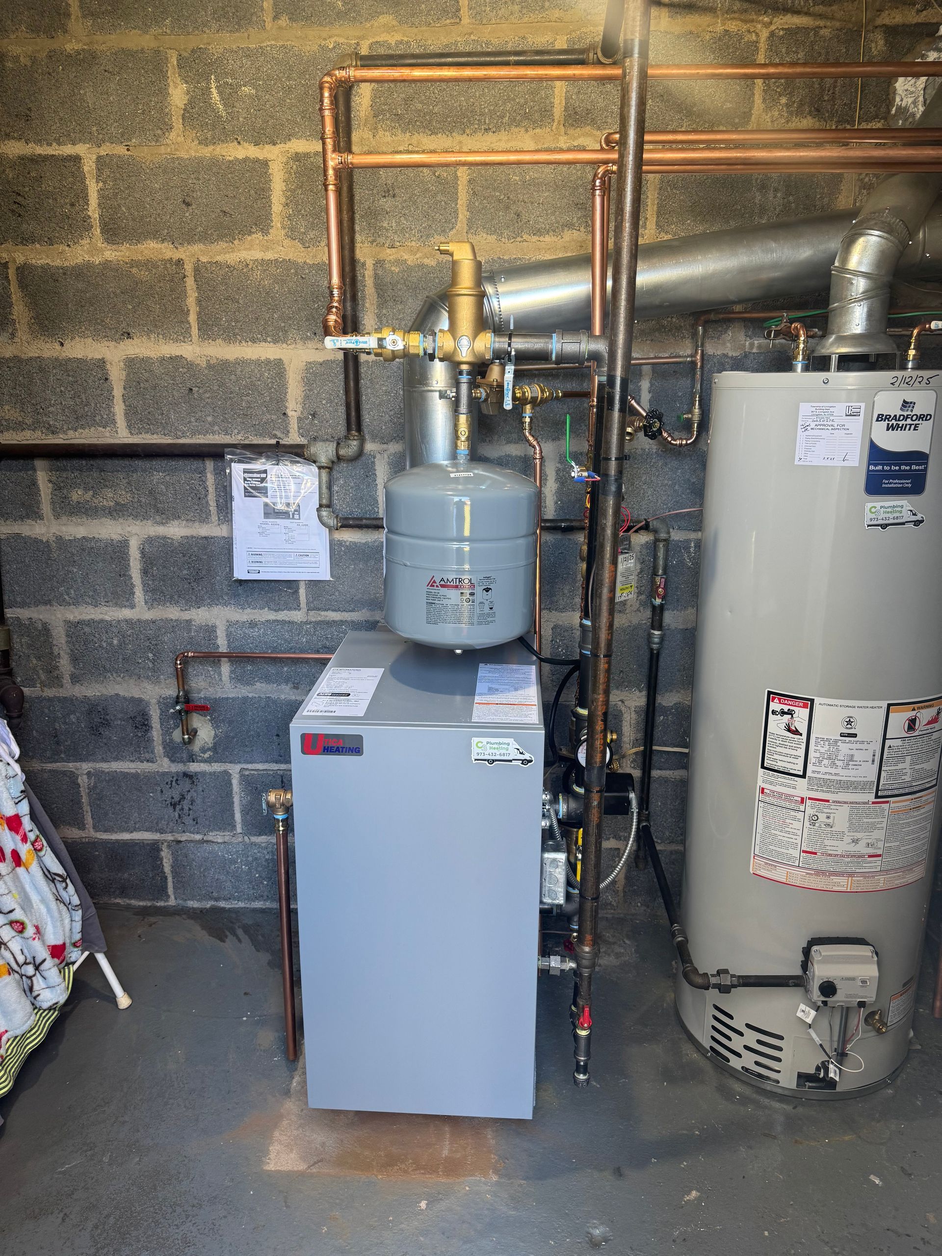 A water heater is sitting in a basement next to a brick wall.