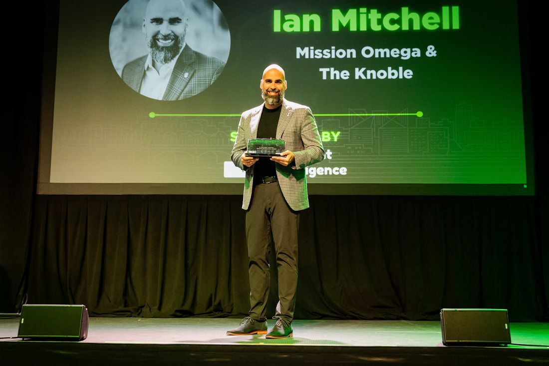 A man is standing on a stage in front of a screen with a picture of him on it.