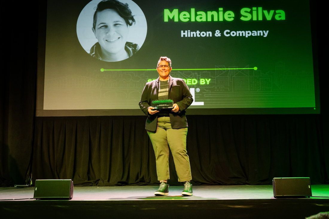 A man is standing on a stage in front of a screen that says melanie silva hinton & company.