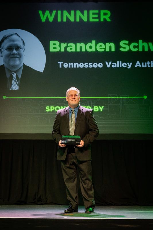 A man in a suit and tie is standing on a stage holding a trophy.