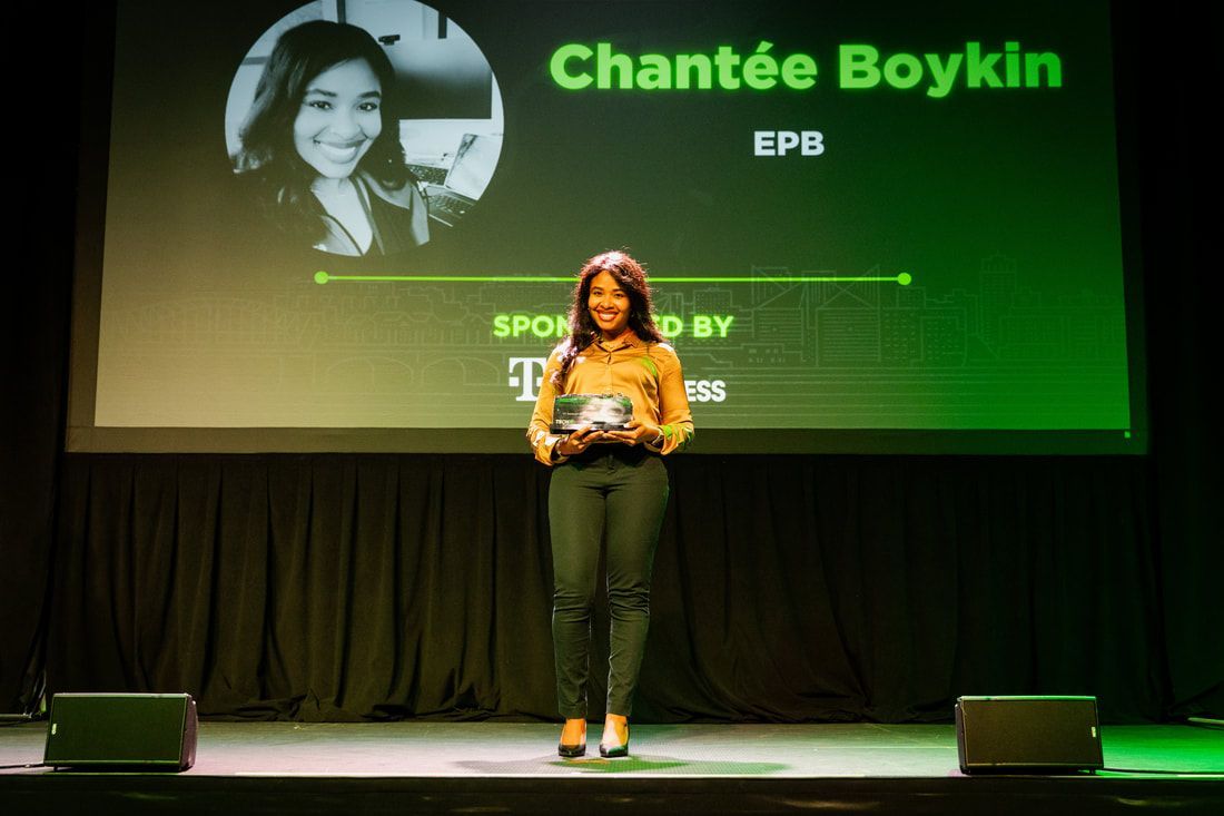 A woman is standing on a stage holding a trophy in front of a large screen.