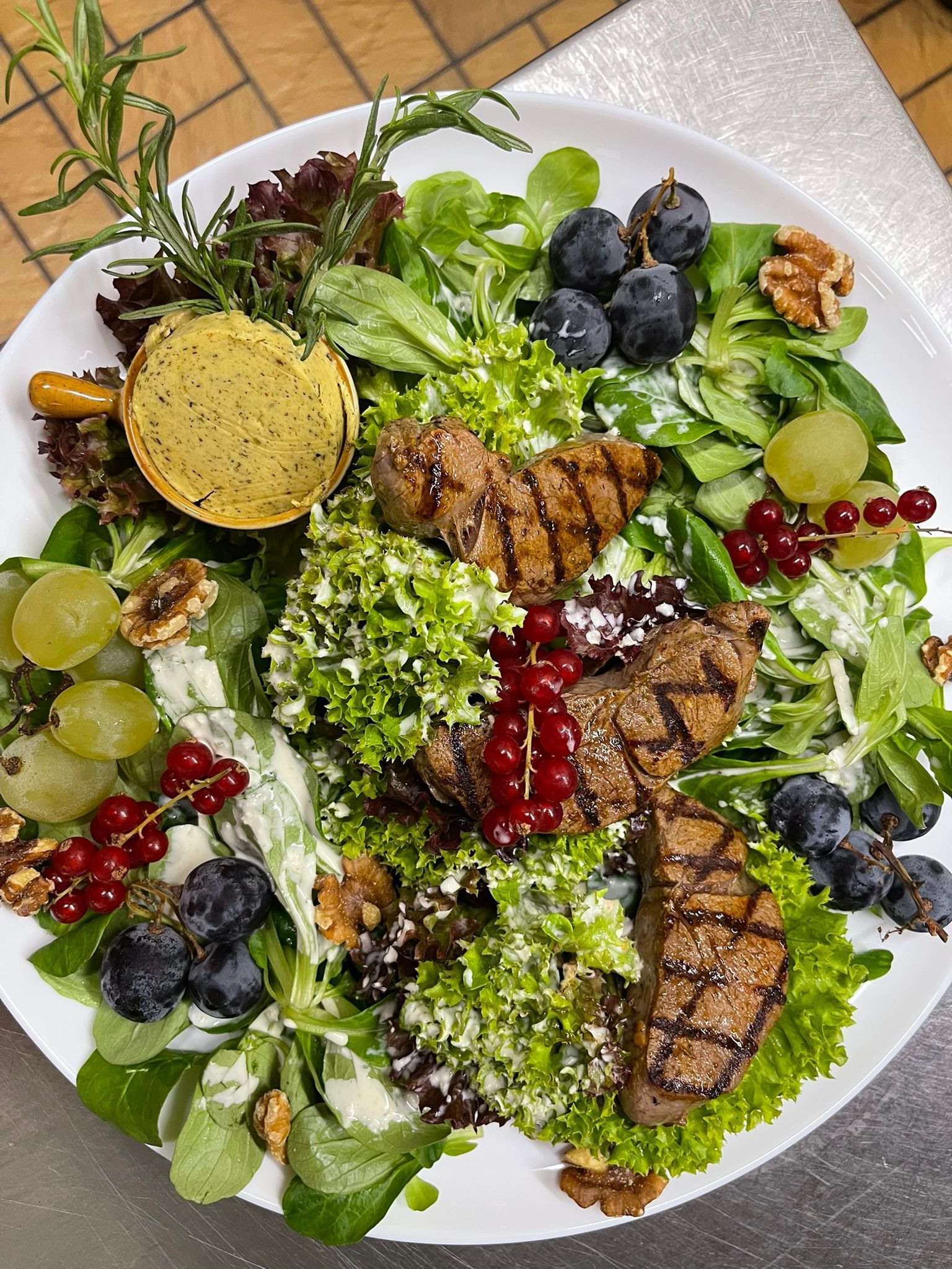 Une assiette blanche garnie d'une salade avec de la viande, des légumes et des fruits.