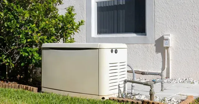 Outdoor beige generator beside a house wall with pipes and vents on a grassy lawn