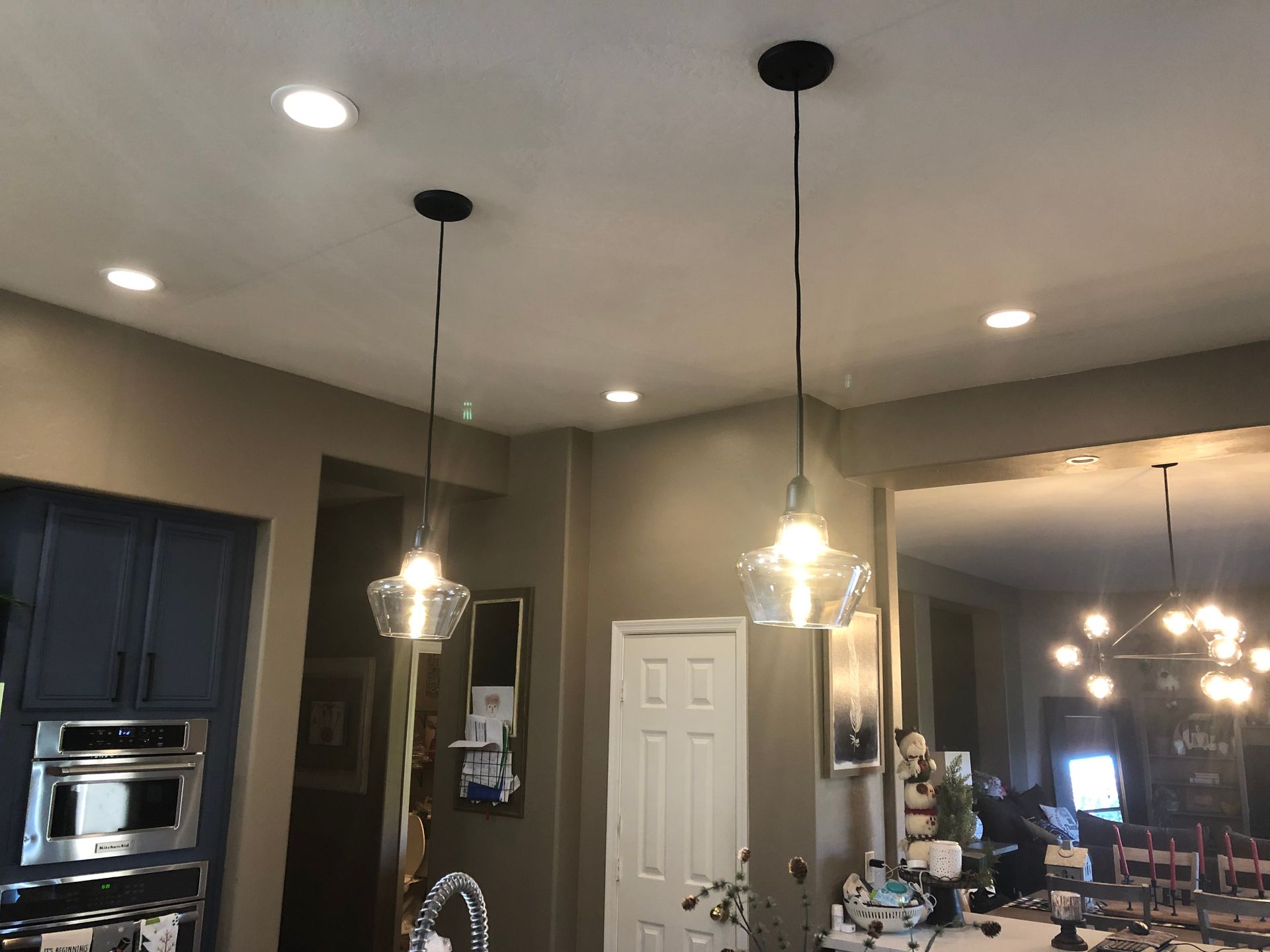 Modern kitchen and dining area with pendant lights, dark cabinets, and a white door in the background