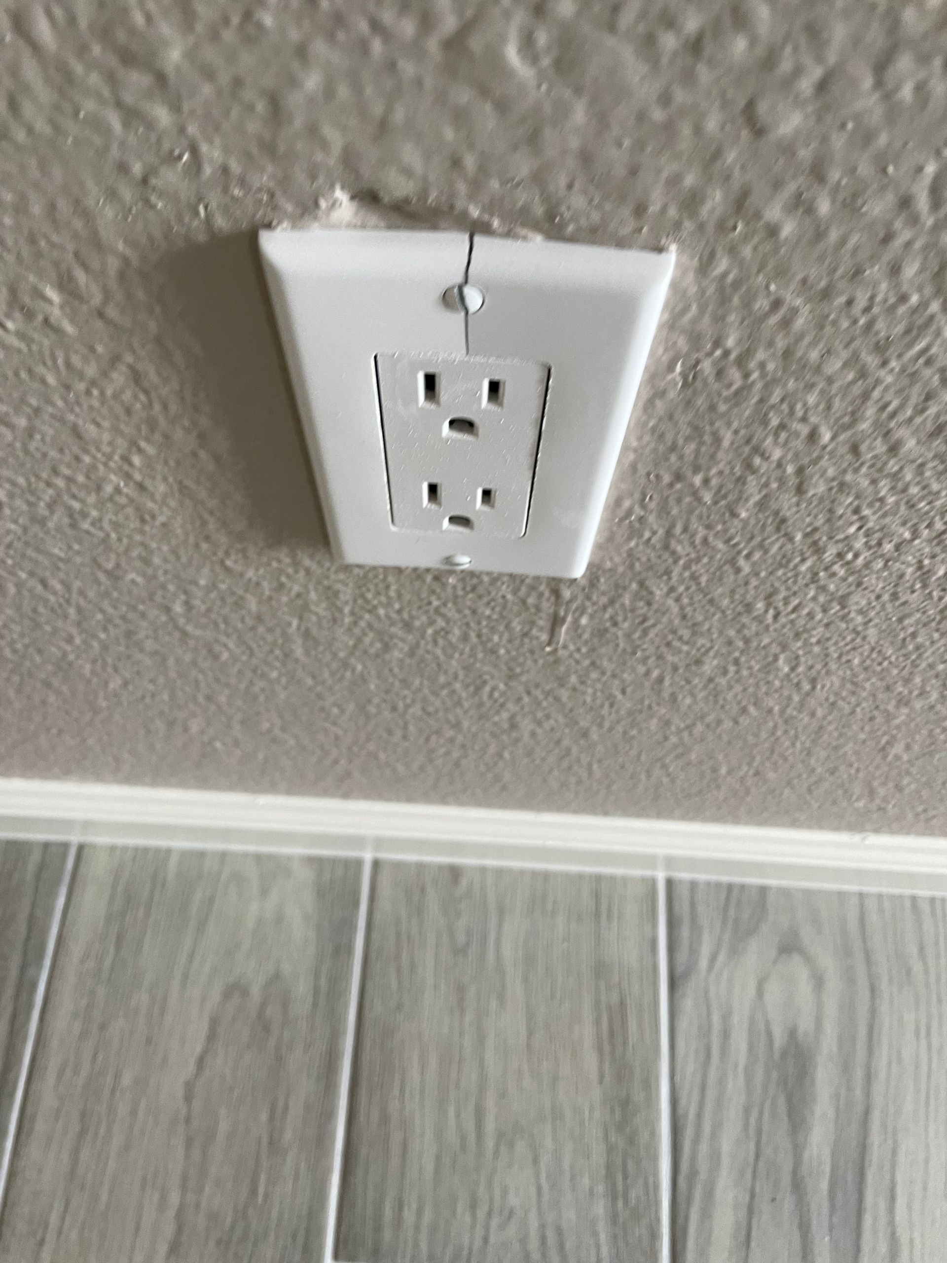 White wall outlet on a beige wall above gray wood flooring, near the baseboard