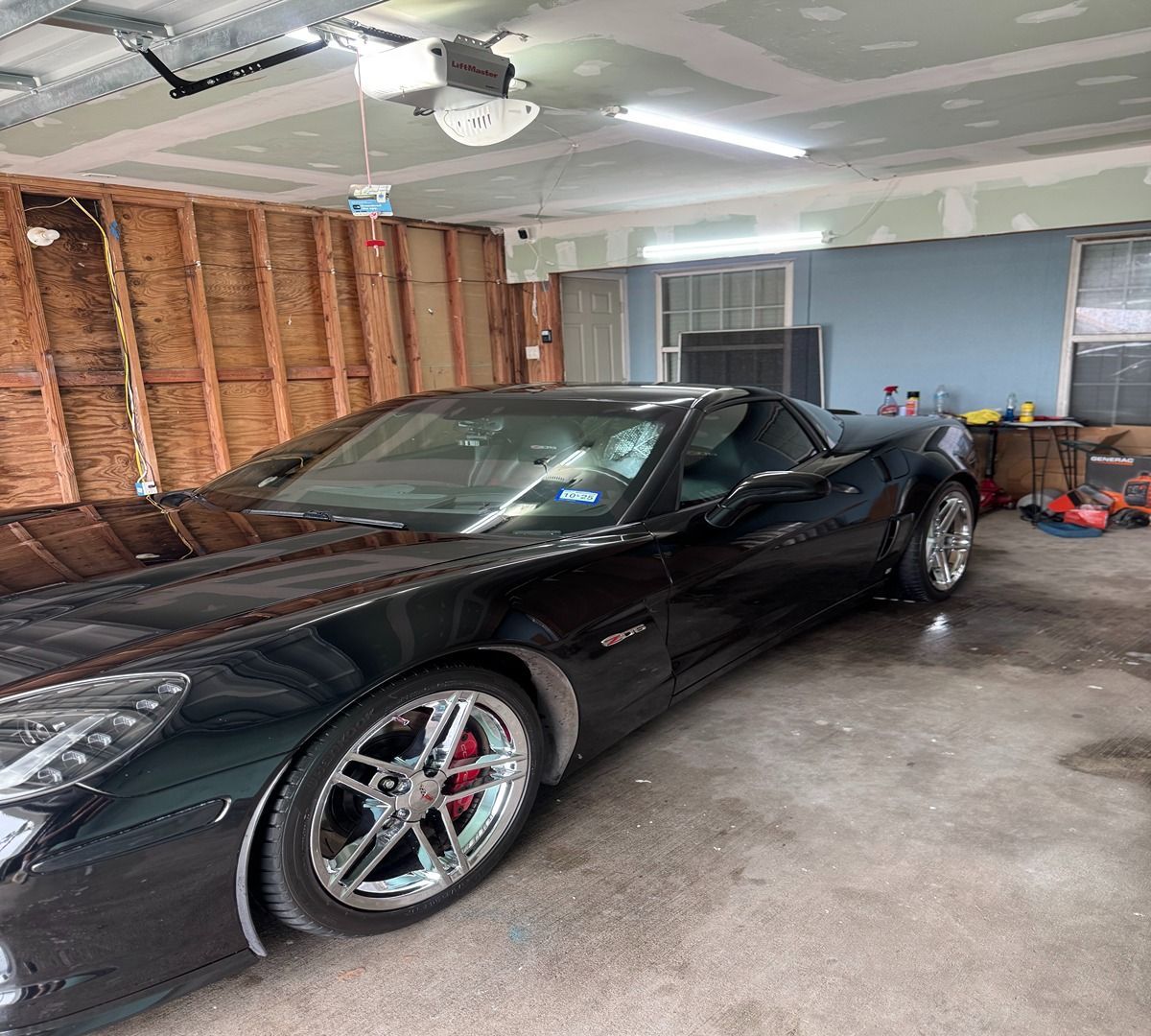 A sleek black sports car parked inside a partially finished garage with wood-paneled walls and a concrete floor.
