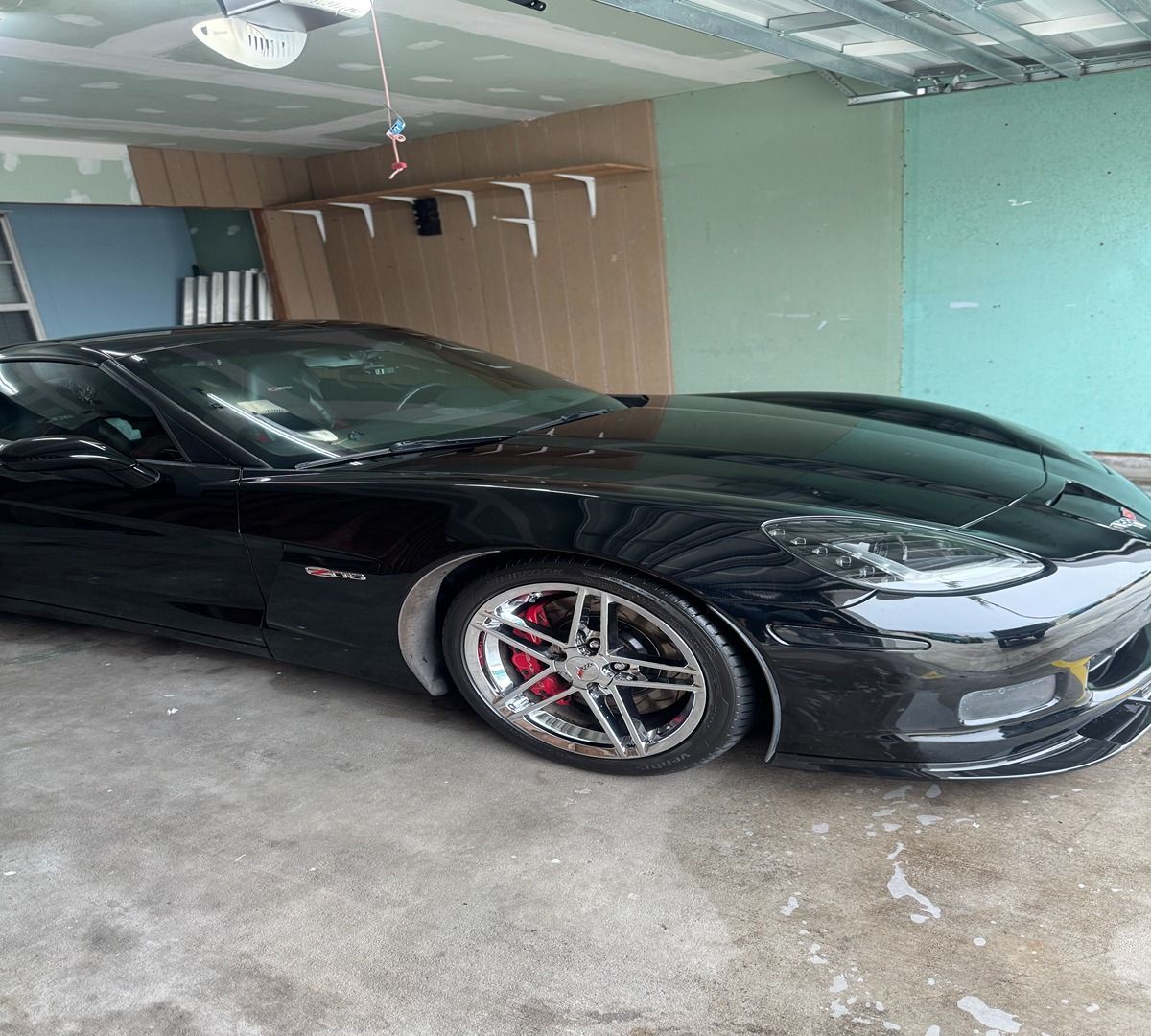 A black Corvette sports car with red brake calipers parked inside a garage.