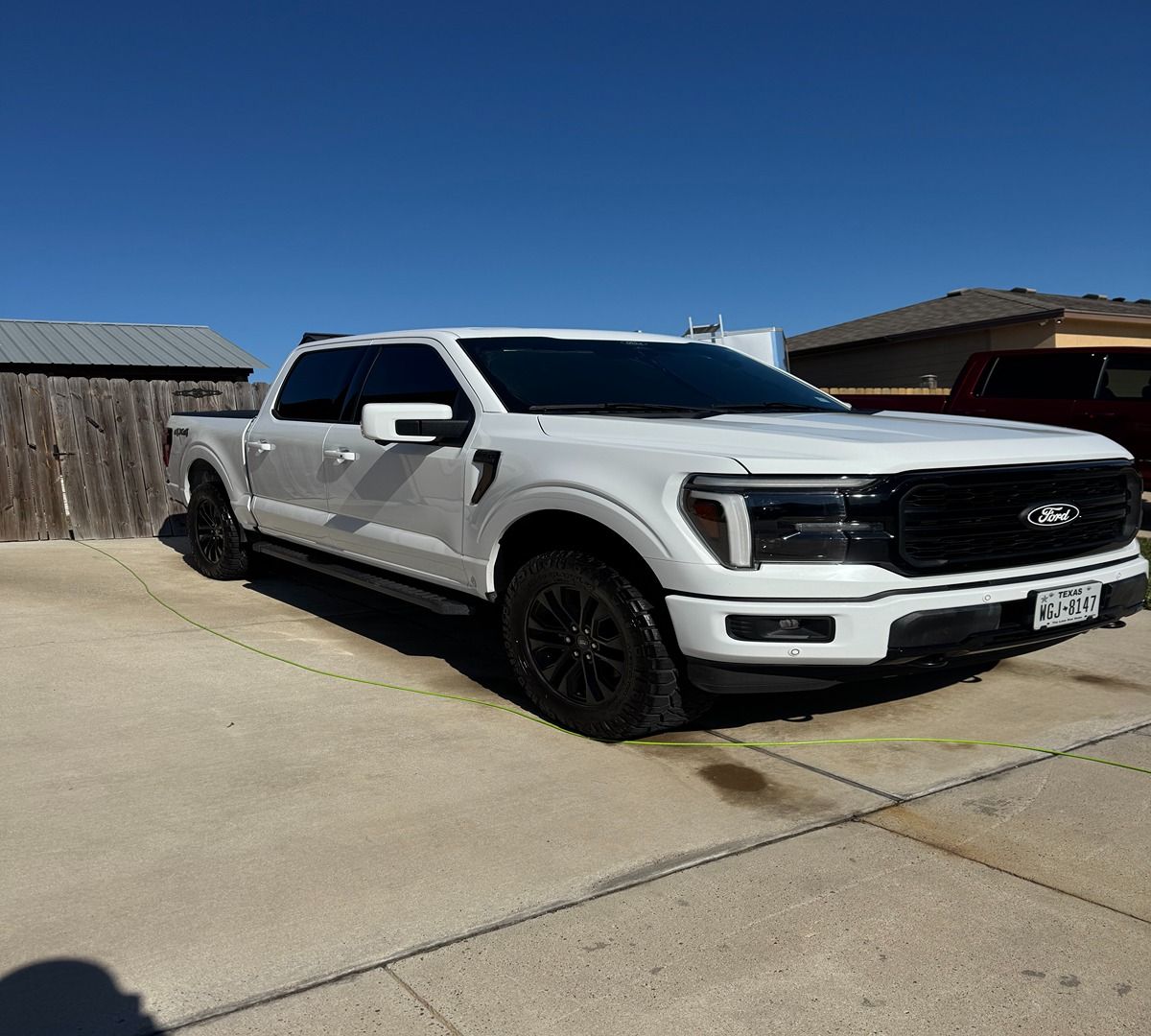 A white Ford F-150 pickup truck with black wheels and a black grille parked on a concrete driveway under a blue sky.