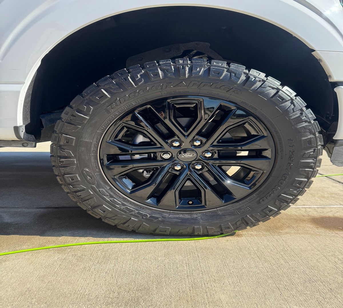 A close-up view of a black, multi-spoke truck wheel with a rugged, all-terrain tire mounted on a white vehicle.