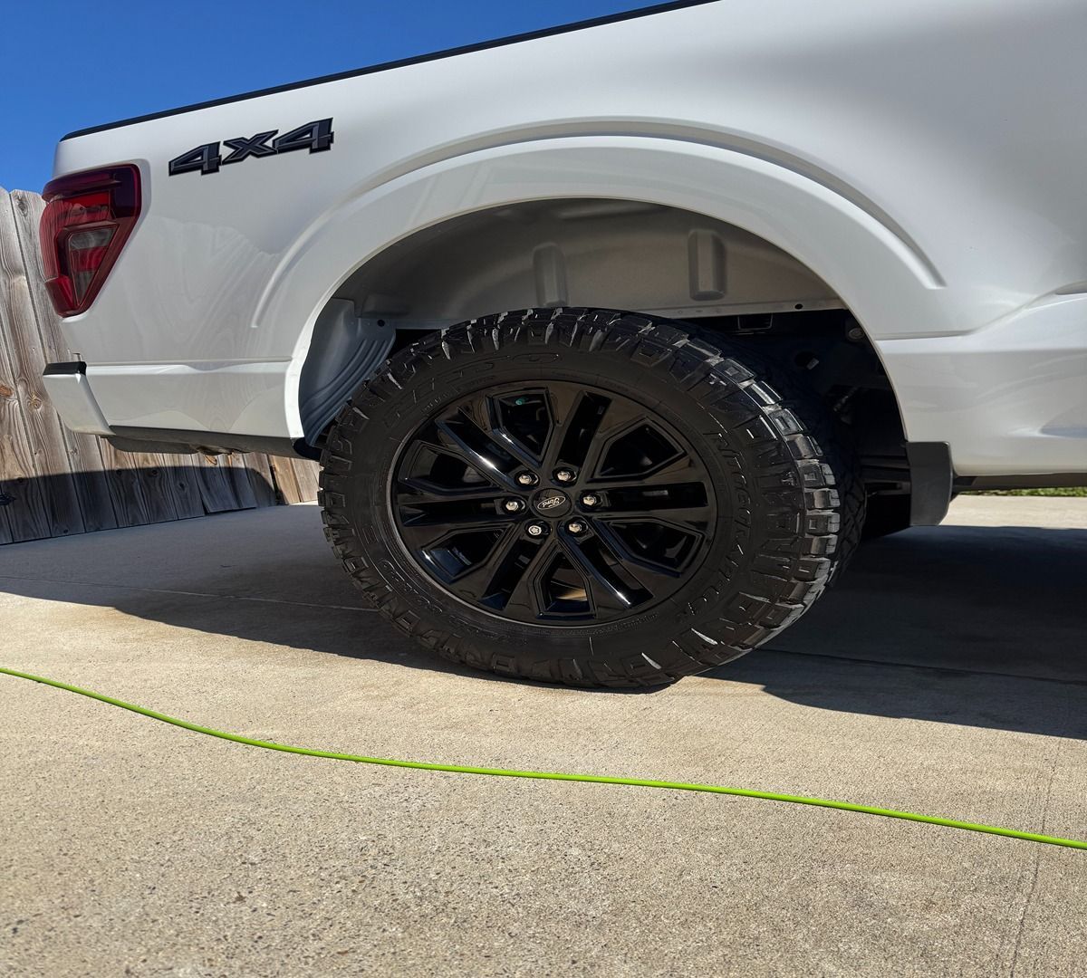 The rear quarter panel and tire of a white pickup truck with a 4x4 emblem on a concrete surface.