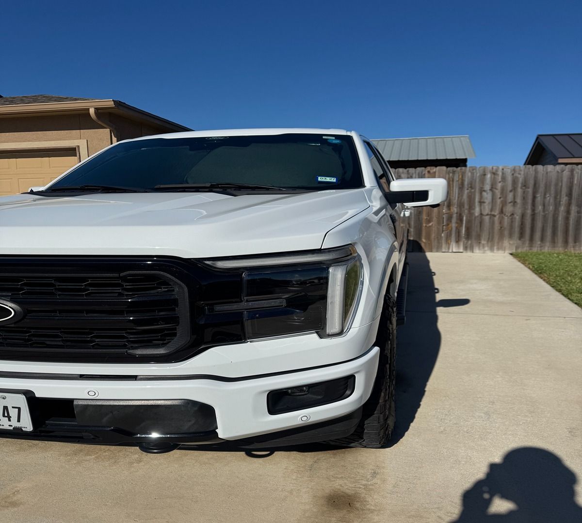 A white Ford F-150 pickup truck parked on a concrete driveway in front of a house under a clear blue sky.